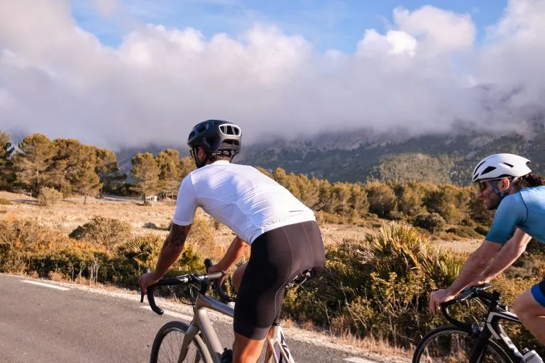 Radfahrer in voller Fahrradausrüstung und Helmen fahren mit ihren Rennrädern auf einer Bergstraße bei Sonnenuntergang. Sportler trainieren hart auf dem Fahrrad im Freien. Spanien