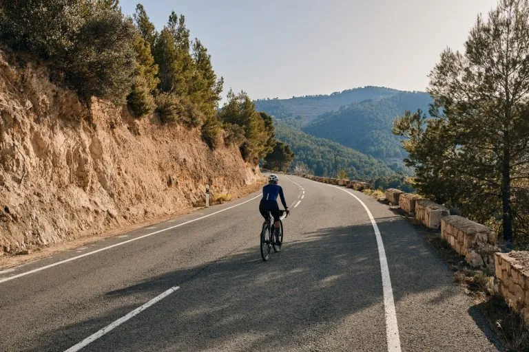 Fit junge Radfahrerin fahren auf der Straße auf einem Kies Fahrrad bei Sonnenuntergang.Silhouette einer weiblichen Radfahrer gegen ein Gebirge Hintergrund.Alicante Region in Spanien